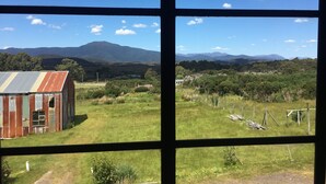 A view through a window with a rural landscape, including a barn and distant mountains. - SeaHen Lodge - entire house - rustic farmhouse charm with amazing mountain views (Zeehan)