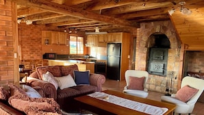 A cozy living room with a sofa, chairs, and a coffee table. A kitchen with a refrigerator and cabinets is visible in the background. - SeaHen Lodge - entire house - rustic farmhouse charm with amazing mountain views (Zeehan)