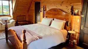 A wooden cabin bedroom with a large bed, a chair, a nightstand, and a lamp. - SeaHen Lodge - entire house - rustic farmhouse charm with amazing mountain views (Zeehan)