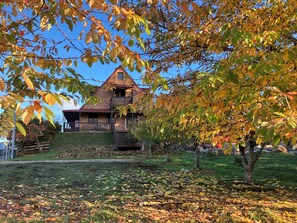 A two-story house with a balcony, surrounded by autumn leaves and a stone wall.