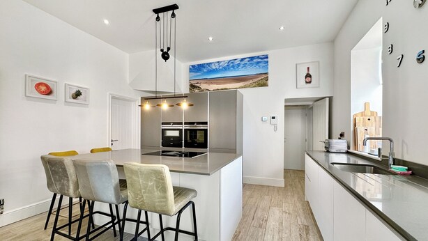 Cozinha moderna com ilha central, banquetas e luminária pendente.