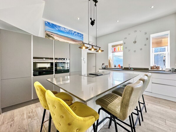 A modern kitchen with a large island, built-in ovens, and a hanging light fixture.