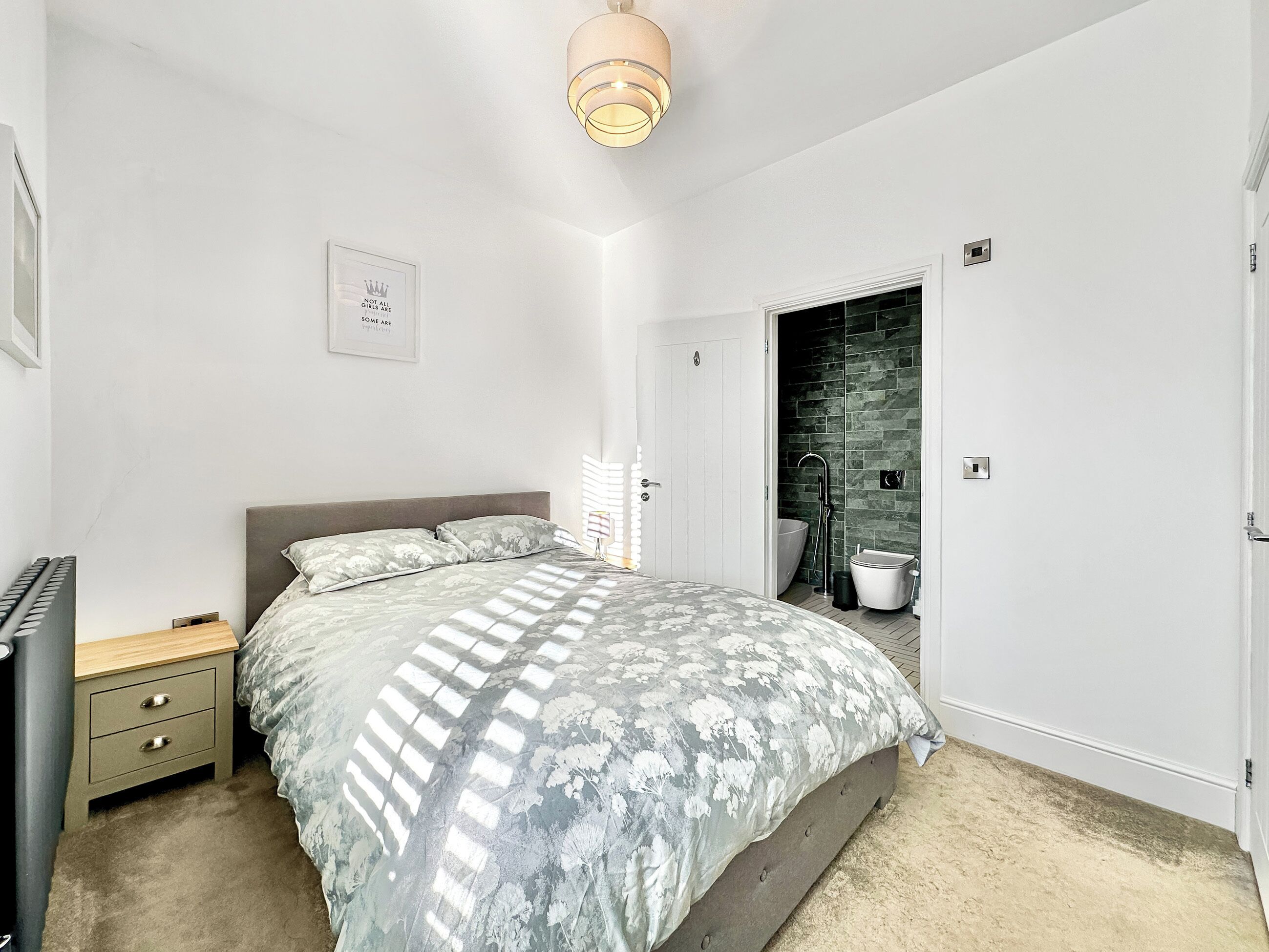 A bedroom with a bed, bedside table, and a bathroom with a bathtub and shower.