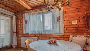 A cozy wooden cabin interior with a round dining table, chairs, a chandelier, and a window with decorative curtains. - Quaint holiday home with garden and views (Oberndorf in Tirol)