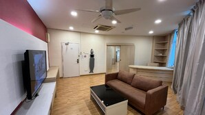 Ein modernes Wohnzimmer mit einem Flachbildfernseher, einem Deckenventilator, einem Sofa, einem Couchtisch und einer Schiebetür, die in einen anderen Raum führt.
