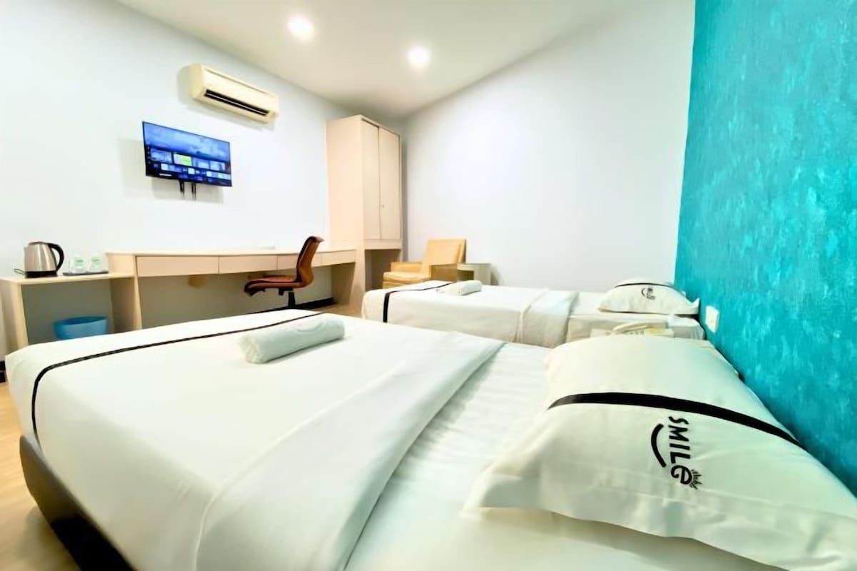 Une chambre d’hôtel avec deux lits, un bureau, une chaise, une télévision et un mur d’accent bleu.