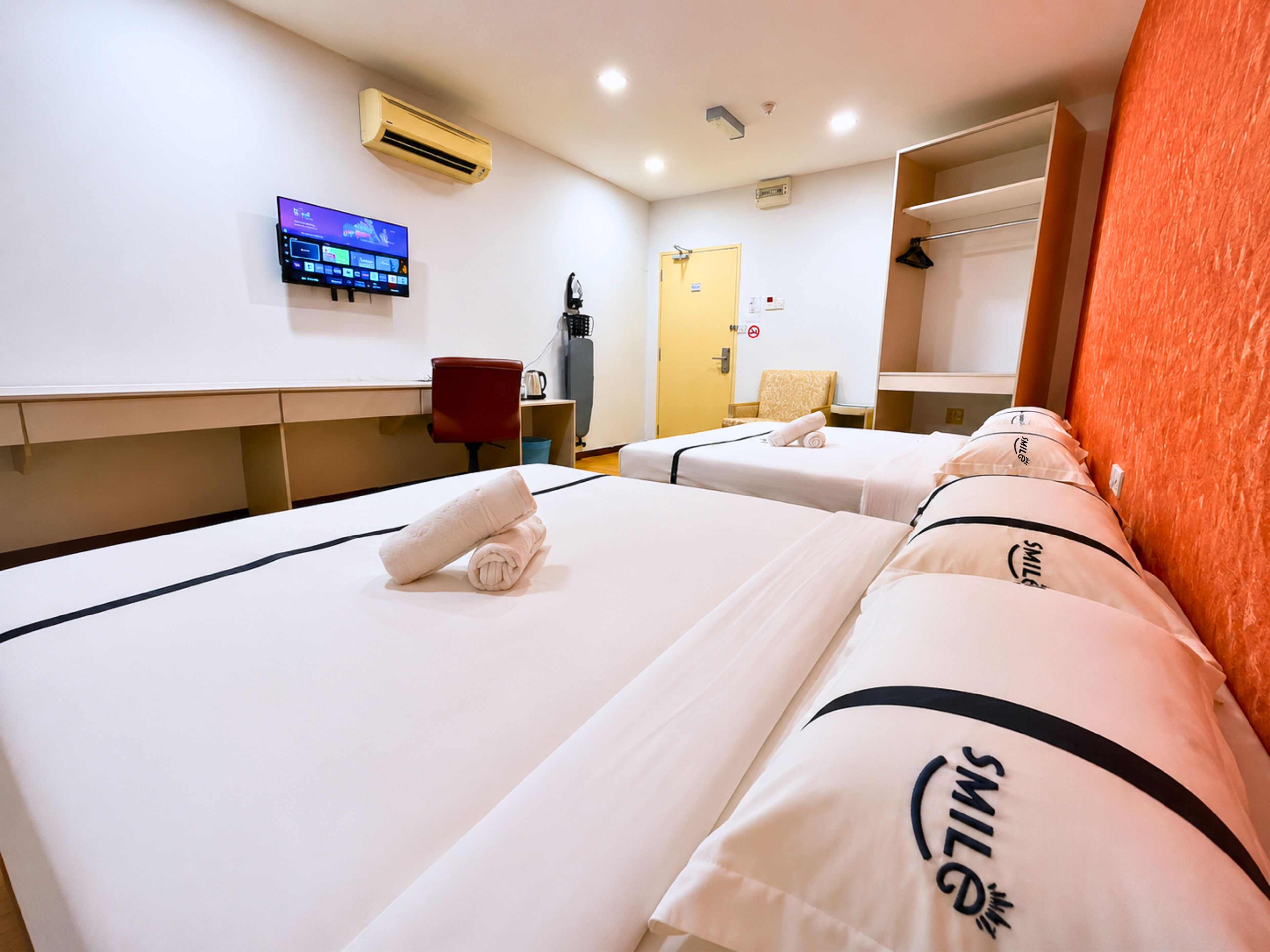 Habitación de hotel con dos camas, un televisor montado en la pared, un equipo de aire acondicionado y una puerta con letrero de 'no admitidos'.