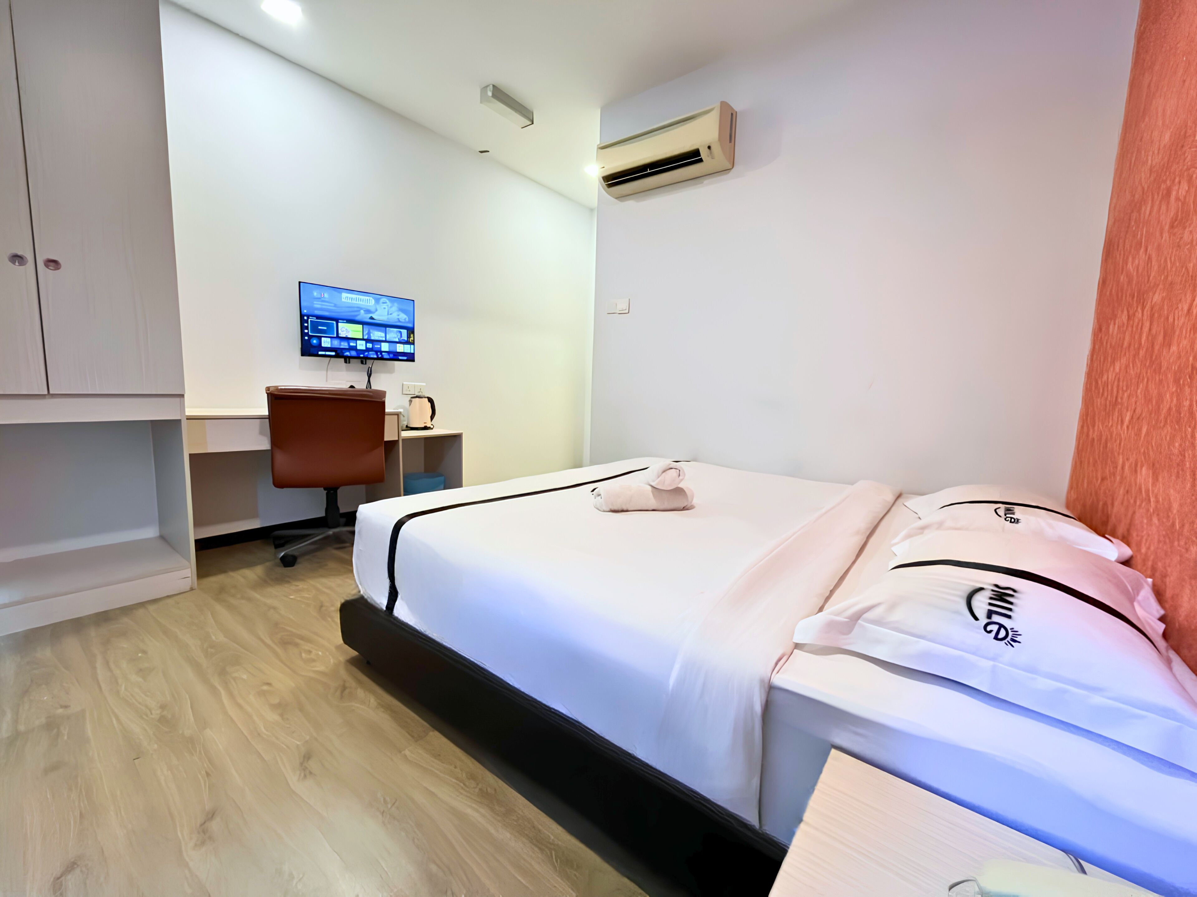A hotel room with a bed, a desk with a chair, a television, and an air conditioning unit.
