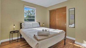 Una camera da letto con un letto, un comodino, una finestra e una porta in legno.