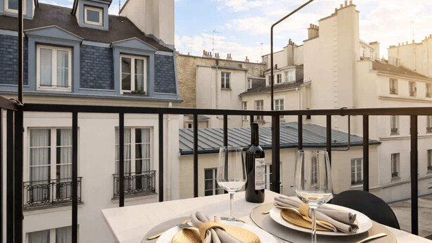 A balcony with a table set for two, overlooking a row of townhouses. - Place des Vosges - Deluxe apartment for 4 (Paris)