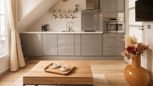 A modern kitchen with a sloped ceiling, built-in appliances, and a wooden dining table with a tray. - Place des Vosges - Deluxe apartment for 4 (Paris)