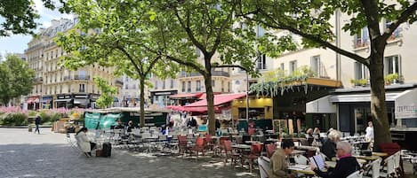 An outdoor café with tables and chairs, surrounded by trees and buildings.
