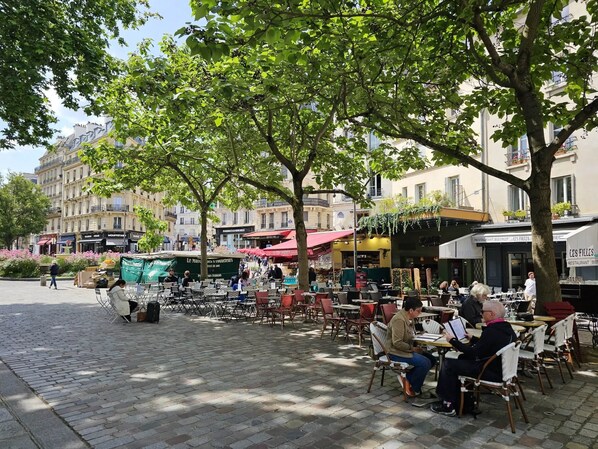 An outdoor café with tables and chairs, surrounded by trees and buildings.