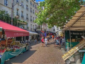 A pedestrian street with market stalls, a red awning, and a building with balconies.