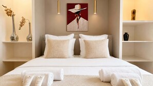 Habitación de hotel con cama, dos mesitas de noche, un cuadro y un florero con flores.