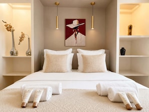A hotel room with a bed, two bedside tables, a painting, and a vase with flowers.