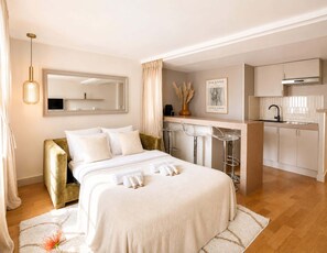 A hotel room with a bed, a sitting area with a chair, a small kitchen area, and a mirror on the wall. - Stylish apartment near the Panthéon (Paris)