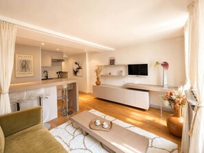 A modern living room with a sofa, coffee table, and a kitchen area with a bar and dining space.