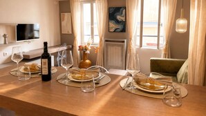 Comedor con mesa de madera dispuesta para cuatro, una botella de vino y un florero con flores.