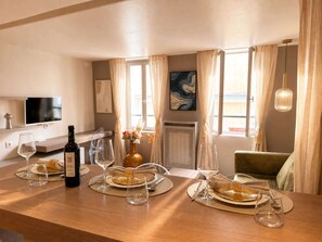 A dining area with a wooden table set for four, a bottle of wine, and a vase with flowers.