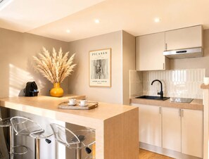 A modern kitchen with a central island, bar stools, a sink, and a framed artwork on the wall. - Stylish apartment near the Panthéon (Paris)