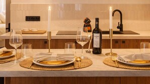 A modern kitchen with wooden cabinets, a white countertop, and a dining setup with plates, glasses, and a bottle of wine. - Marais stylish & central studio (Paris)