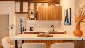 A modern kitchen with wooden cabinets, a central island with bar stools, and a decorative vase. - Marais stylish & central studio (Paris)