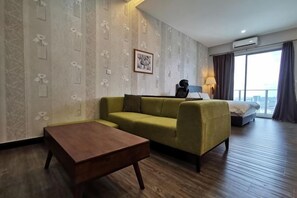 A hotel room with a green sofa, a wooden coffee table, a bed with a white comforter, and a large window with curtains. - Mykey Silverscape B-39-06 Melaka City (Melaka)