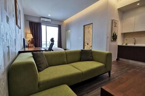 Un salon comprenant un canapé, une table basse en bois, un bureau avec une chaise, et une vue sur l’extérieur par une fenêtre.