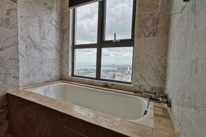 A bathroom with a bathtub, a window with a city view, marble walls, and a shower area. - Mykey Silverscape B-39-06 Melaka City (Melaka)