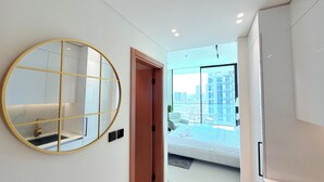 A modern hotel room with a large round mirror, a bed with a city view, and a small balcony. - Premium Studio In Jvc Bazr (Dubai)