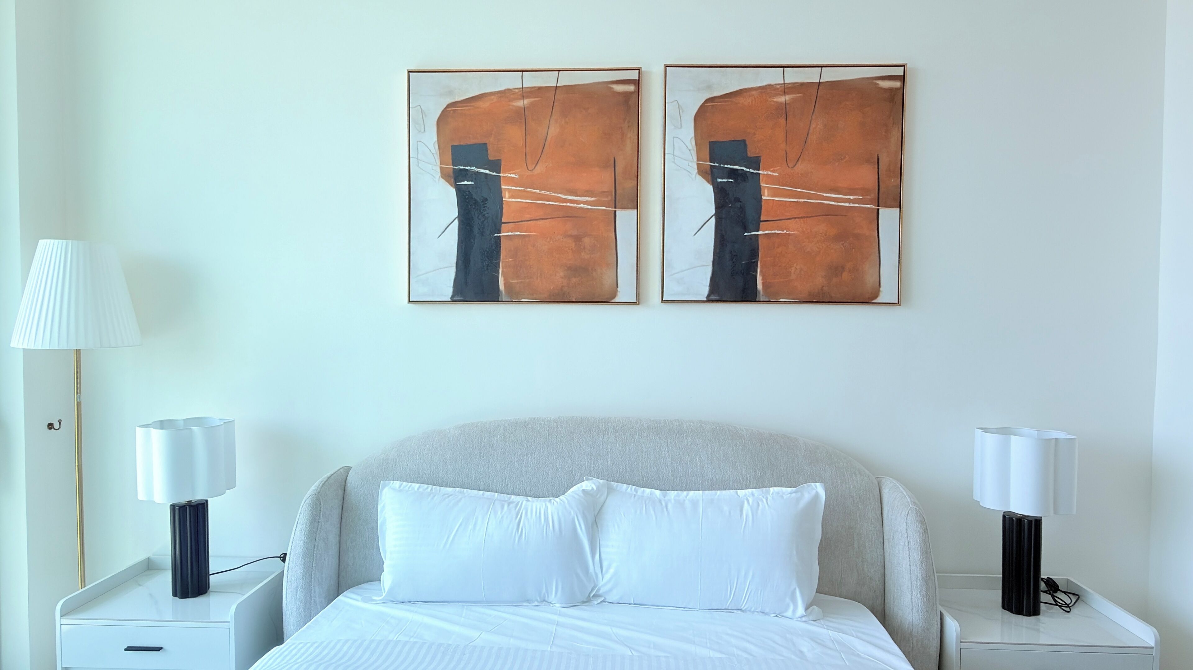Habitación de hotel con una cama, dos mesitas de noche, una lámpara y dos cuadros abstractos en la pared.