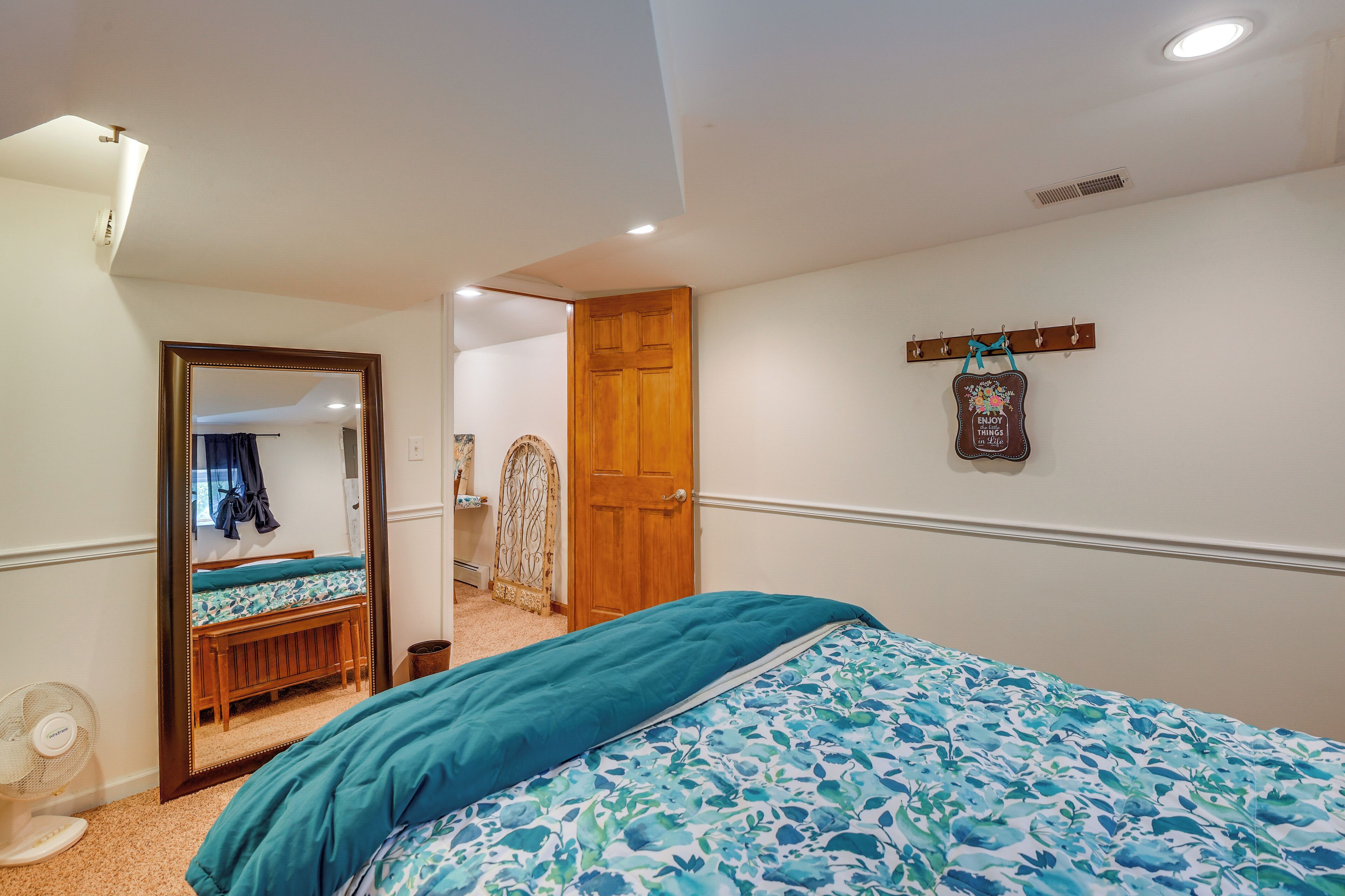 A bedroom with a bed, a wooden door, a mirror, and a wall-mounted coat rack.