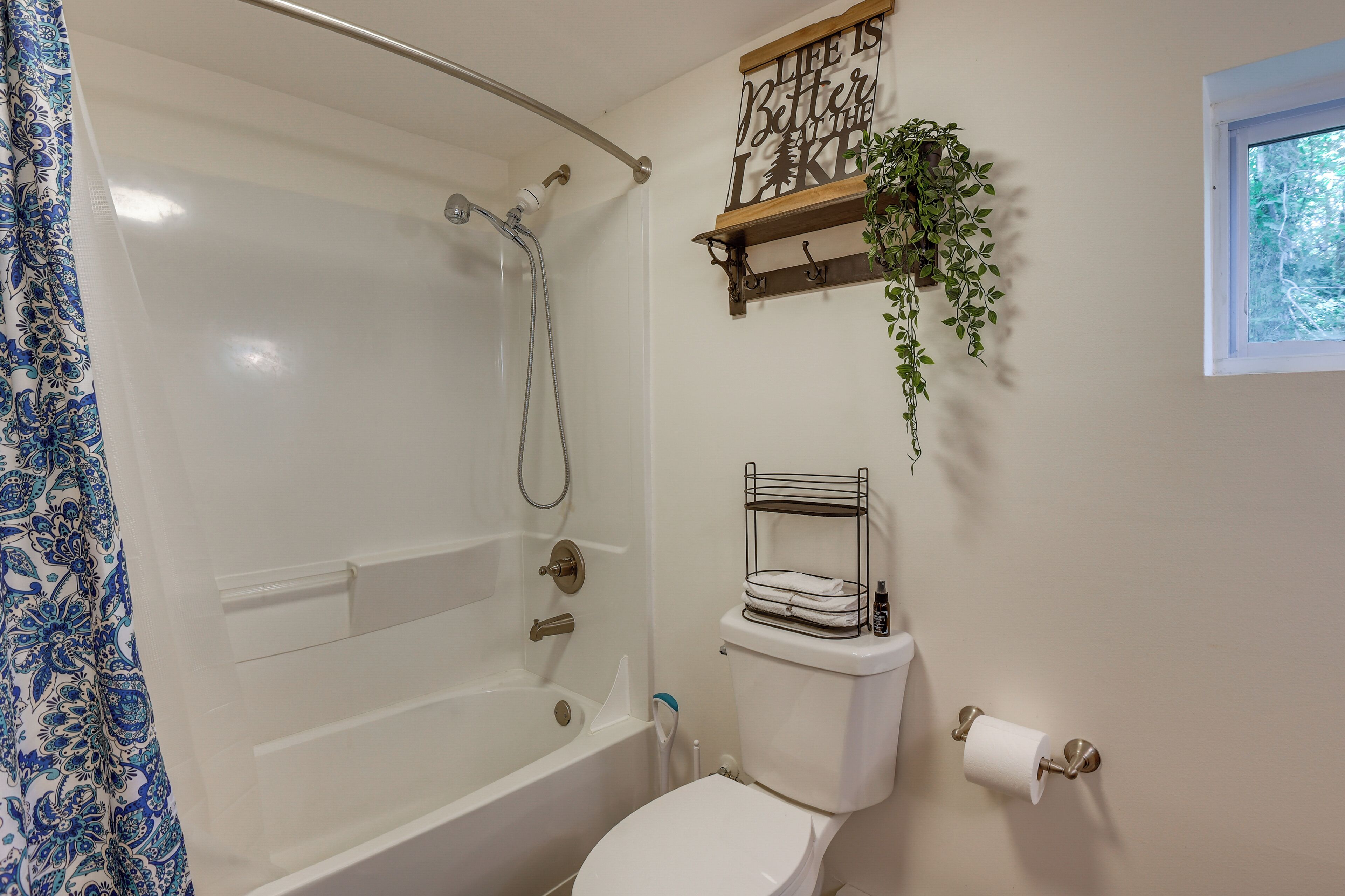 A bathroom with a bathtub, toilet, and a shower. There is a shelf with a plant and a sign above the toilet.