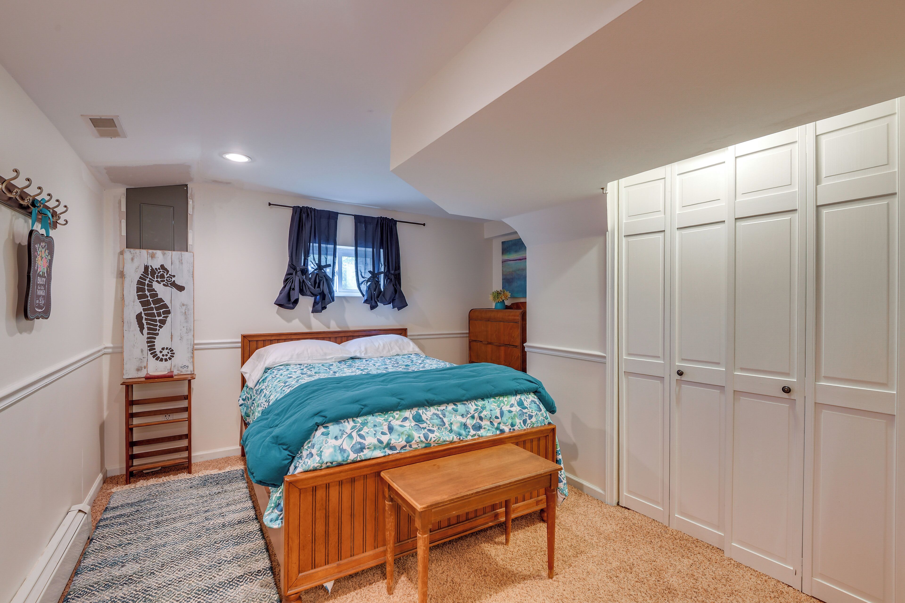 A bedroom with a wooden bed, a bench, a small table, a wardrobe, and a window with curtains.