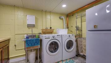 Une buanderie équipée de deux machines à laver à chargement frontal, d’un évier avec une serviette bleue, d’une armoire blanche et d’un paillasson.