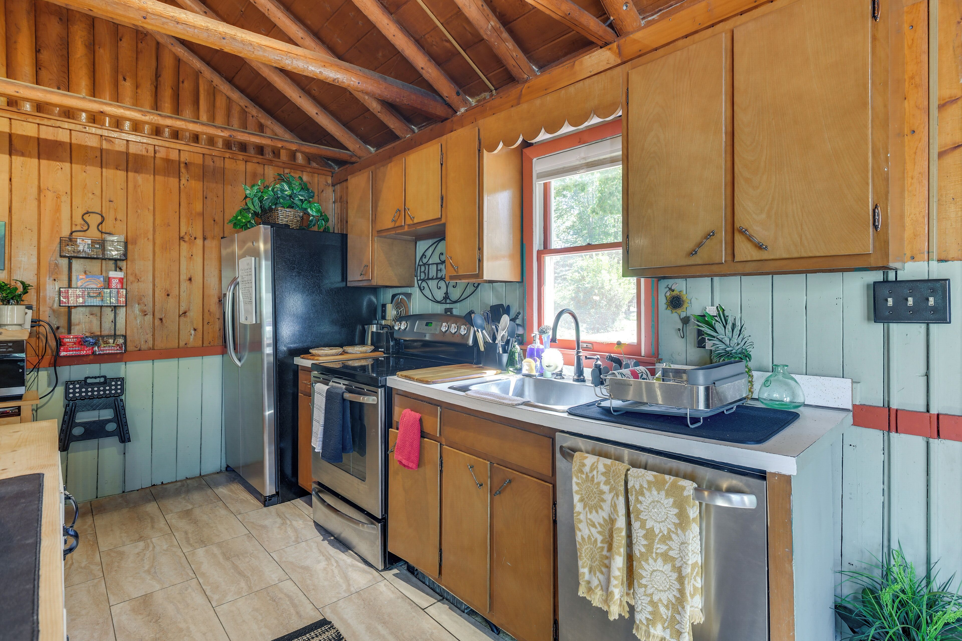A kitchen with wooden cabinets, a stainless steel refrigerator, a sink, and a window.