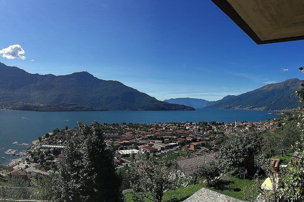 Een panoramisch uitzicht op een stad aan een meer, met bergen op de achtergrond, met een mix van woon- en bedrijfsgebouwen.