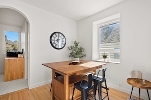 Uma área de refeições com uma mesa de madeira, cadeiras pretas, um relógio e um vaso de planta.