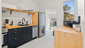 A modern kitchen with black cabinets, a wooden countertop, and a stainless steel refrigerator.