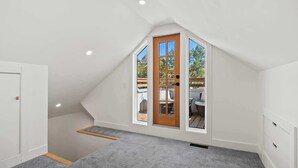 Una stanza con soffitto spiovente, una porta in legno con vetrate e vista su una terrazza esterna.