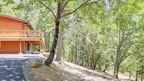 Una cabaña de troncos de dos pisos con un balcón, rodeada de un bosque frondoso.