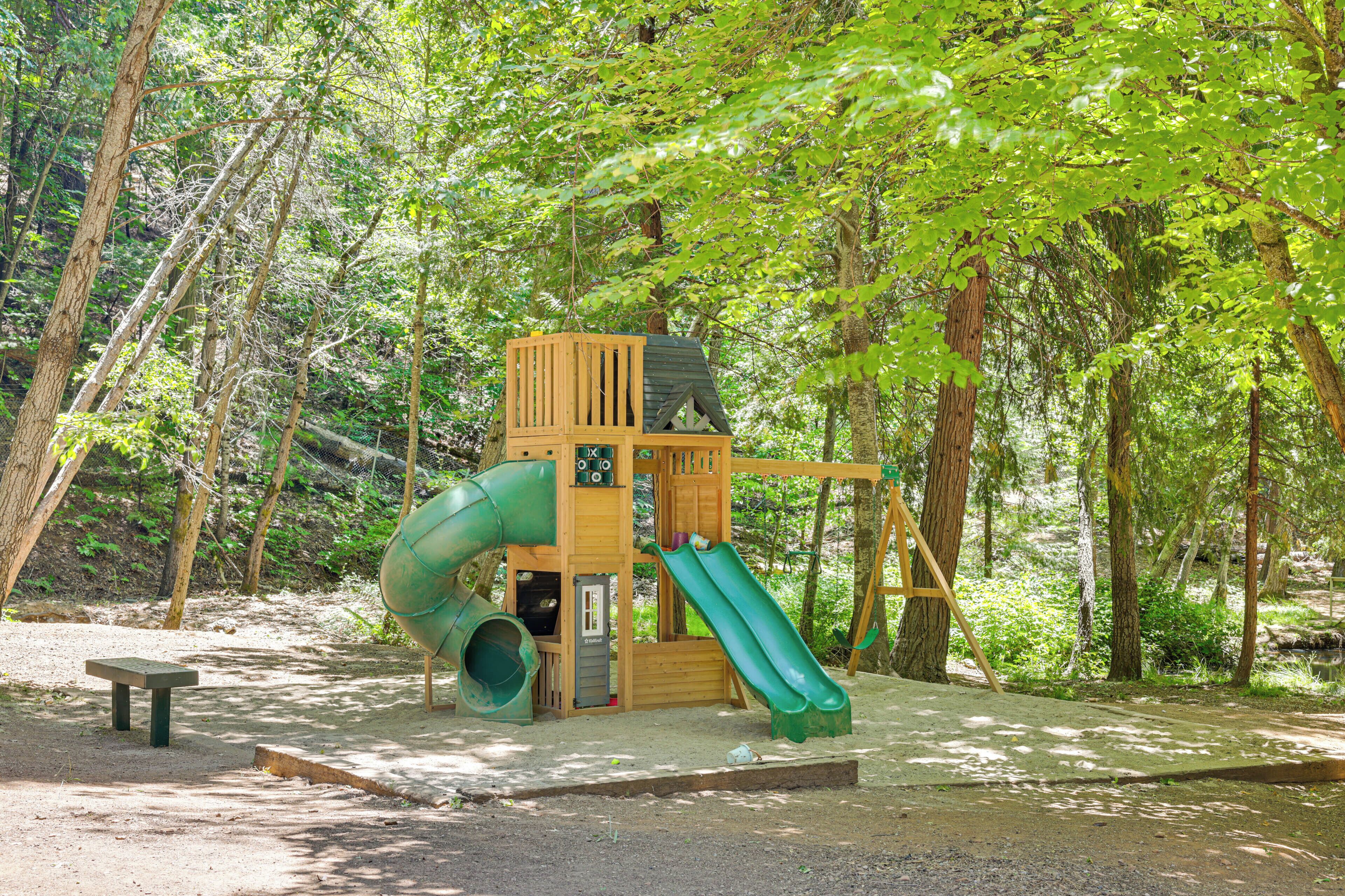 A wooden play structure with a slide and a climbing wall in a wooded area.