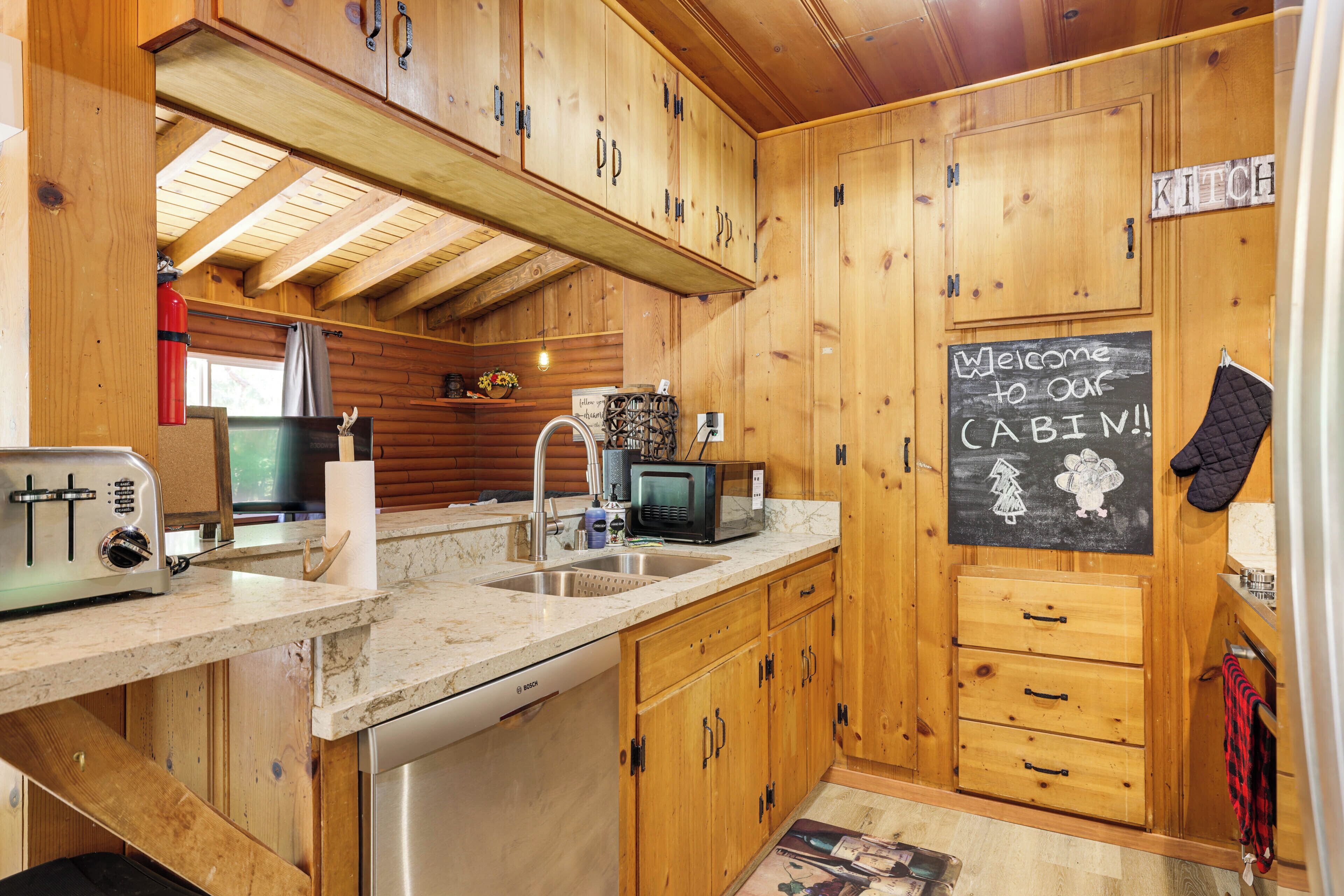 A wooden cabin kitchen with a toaster, sink, microwave, and a chalkboard sign.