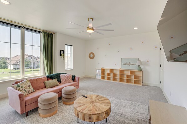 A spacious living room with a large window, a ceiling fan, a wooden coffee table, and a pink sofa. - Luxe Retreat w/ Patio & Fenced Yard in Waxahachie! (Waxahachie)