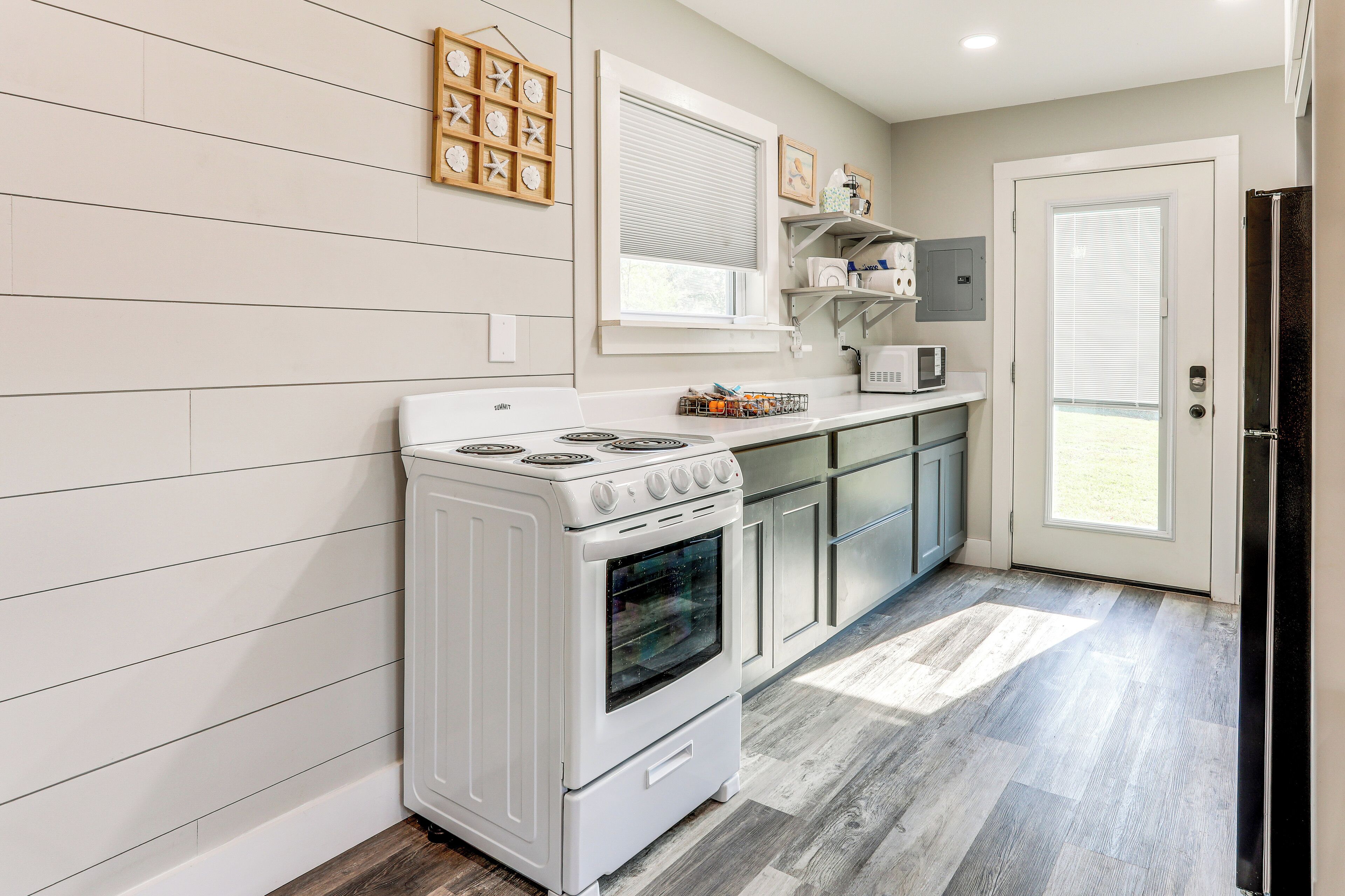 Una cucina moderna con piano cottura bianco, rivestimenti in legno, una finestra e una porta che dà su un balcone.