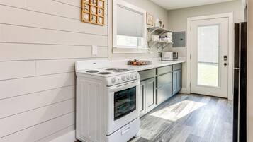 Una cucina moderna con piano cottura bianco, rivestimenti in legno, una finestra e una porta che dà su un balcone.