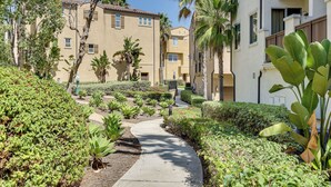 A pathway flanked by lush greenery and palm trees, leading to a multi-story building with balconies. - Oceanside Extended Stay Near Camp Pendleton (Oceanside)