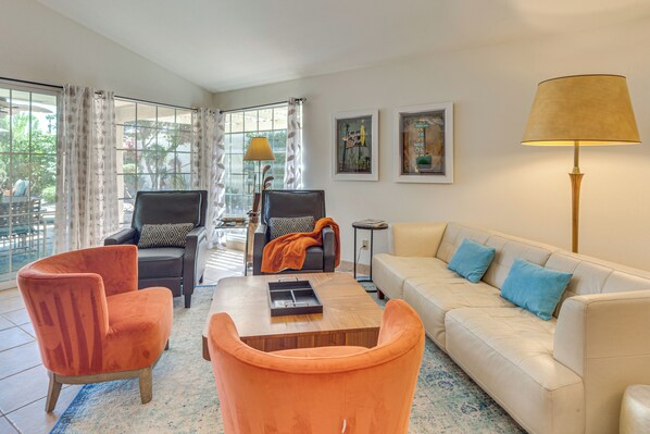Uma sala de estar moderna com um sofá bege, poltronas laranjas, uma mesa de centro de madeira e um abajur.