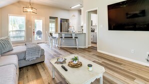 Een moderne woonkamer met een grijze bank, een salontafel met decoratieve voorwerpen, en een keuken op de achtergrond.